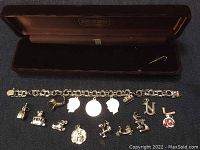 Charm bracelet displayed with 14 various charms laid out and bracelet in jewelry box