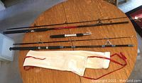 Full view of three fishing rods laid on a wooden table with one white cloth rod sleeve
