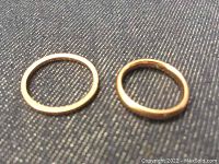 Two gold band rings on blue fabric background, narrow ring left, wider ring right