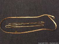 Overview of two necklaces on dark fabric background showing both chains laid out in full lengths