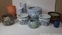 Full view of assortment including terracotta pots, white trays, floral porcelain pots, blue small pot, decorative metal and glass container, brown glazed pots