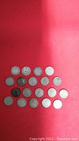 19 Canadian 10 cent pieces arranged on red cloth in 4 rows showing fronts with various degrees of wear and patina.