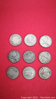 Photo showing all nine Canadian silver 25 cent coins arranged in three rows on red background, displaying wear and some tarnishing.
