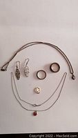 Full view of all jewelry items included in lot arranged flat: two necklaces, two rings, earrings, and pendant.