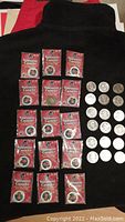 Two groups of Vancouver Canucks collectible coins. Fifteen coins in sealed red packages labeled as 2002/03 season medallions arranged on the left, and eighteen loose silver coins arranged in three rows on the right.