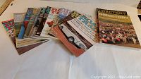 Set of 13 vintage car magazines laid out in a row, showing colorful covers with various cars and racing scenes from 1960-1962