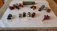 Wide view of all included diecast cars, trucks, buses, and aircraft, displayed on white surface with labels of brand names visible beneath certain items. Includes F-15 Eagle jet, various buses, trucks, and cars.