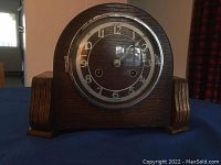 Front view of vintage wooden mantle clock with round face and Arabic numerals, glass covered, in dark wood case.
