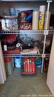 Overall closet shelf view showing Christmas tins, cleaning products, miscellaneous items, and boxed flatware set on floor.