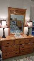 Full view of wood finish dresser with attached mirror, holding two table lamps and decorative items, showing condition and overall style.