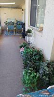View of the plant stand with faux florals arranged beside a window, outdoor carpeted porch setting with patio chairs in background