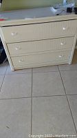 Front view of the white faux wicker 3-drawer dresser showing three drawers with white handles and textured front panels.