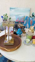 Photo of assorted decorative and game items on round white table including hourglass, candles, ceramic figurines, and tray