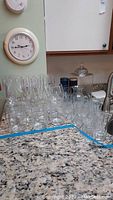 Countertop with multiple clear glassware including drinking glasses of various sizes, champagne flutes, and a cut glass vase visible at the side.
