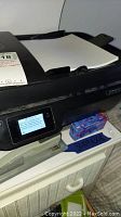 Close-up of HP OfficeJet 3830 printer touchscreen with paper loaded in input tray