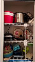 Kitchen shelves with red and white Igloo cooler, stainless steel Rival Crock-Pot, metal bundt pan, glass and plastic dishes visible.