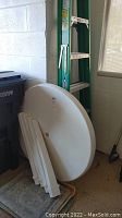 Green Werner branded 6 ft step ladder next to white round plastic table parts and a small patterned area rug.