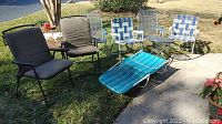Wide shot of all lawn patio chairs and table showing arrangement on grass and sidewalk, displaying all items in the lot