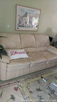 Front and full view of beige leather sleeper sofa with cushion seats, armrests and some creasing on cushions.