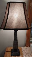 Full view of one night table desk lamp showing beige fabric shade with dark trim and bronze textured base on a wooden surface.