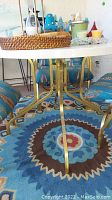 Photo showing round patio table leg detail with gold metal base and blue patterned rug underneath.