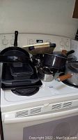Photo showing assorted pots, pans, baking pans and trays stacked on a stove top.