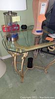 Side table with metal frame and glass top supporting a clear glass surface with gold-tone decorative design on the underside, shown with items placed on top.