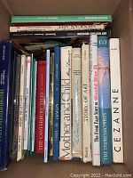 Top view of a cardboard box filled with assorted large books showing titles like 'Mother and Child,' 'Story of Art,' 'The Impressionists,' and 'Cezanne.'
