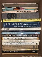 Close-up of the stacked books showing titles related to art, pottery, drawing, ballet, and seamanship.