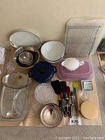 Overview of various kitchen servingware and utensils laid out on table including bowls, trays, platters, and cooking utensils