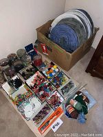 Photo showing multiple compartments of assorted small beads, buttons, and craft items arranged on the floor next to yarn balls and paint pots.