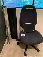 Office chair with MEC laptop case on seat and two projector screens leaning beside chair: older tripod screen and newer black retractable screen