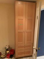 Front view of the wooden wardrobe cabinet showing two paneled doors and two drawers below, with silver-colored handles and knobs.