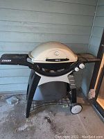 Front view of Weber gas grill showing dome lid, side shelves, control knobs, and wheels.