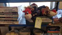Books mainly of Calvin and Hobbes stacked with plush animal toys including a cow and cheetah in a container