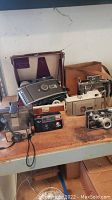 Wide view showing lot of vintage cameras on table, various models including Polaroid and 35mm cameras