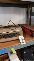 IBM electric typewriter showing keyboard, keys, and plugged power cord on a shelf.