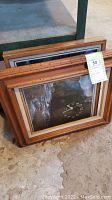 Wood frames stacked with a visible label indicating lot 50, showing framed art with clock