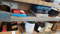 Shelving with stacked tool cases of various sizes and colors along with barrels and cans beneath