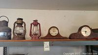 All five items on shelf: three lanterns at left, two mantel clocks at right