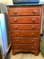 Front view of vintage wooden dresser showing six drawers and round knobs, wood surface has scratches and wear.
