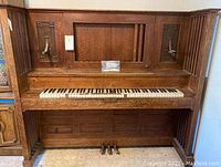 Front view of vintage upright piano showing keyboard with some replacement keys and carved wooden panels.