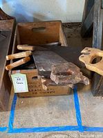 Multiple weathered vintage handsaws with wooden handles and rusted blades in a wooden crate.