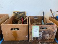 First photo shows two wooden crates filled with assorted hand tools including rusted metal tools and woodworking tools.
