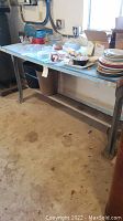 Wood and metal work bench with various household items on top and two metal wastebaskets below.