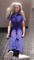 Full body photo of the Bionic Woman action figure seated, wearing purple pantsuit and white shoes, showing bionic chips in the right arm.