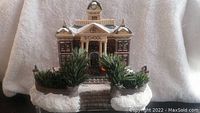 Front view of the Christmas village school building showing snow-covered roof and greenery.