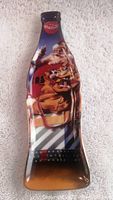 Full view of the Coca-Cola bottle shaped porcelain plate showing Santa Claus holding a Coke bottle with a sack of toys and dolls, with a red Coca-Cola logo at the top.