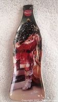 Full view of the porcelain collector plate shaped like a Coca-Cola bottle featuring Santa Claus by the Christmas tree with 'Drink Coca-Cola' logo at the neck.