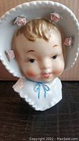 Front view of the vintage baby face head vase showing details of the bonnet with pink roses and blue bow.